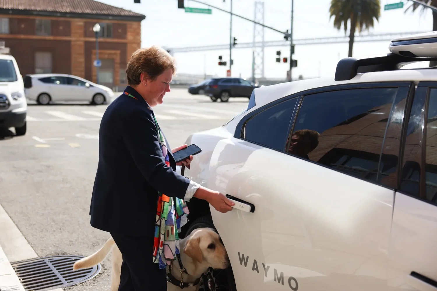 Sharon Giovinazzo, CEO of LightHouse, a nonprofit organization for the blind and visually impaired, opens the door of a Waymo autonomous car with her guide dog Pilot in San Francisco on Monday. | Source:Jeremy Chen/The Standar
