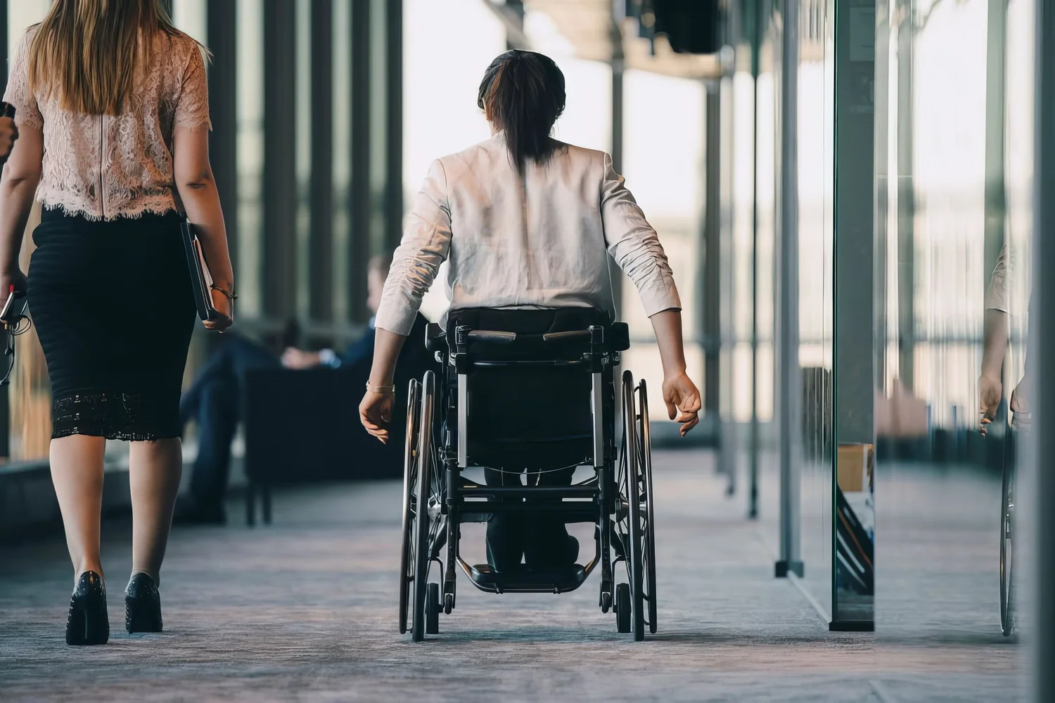 A wheelchair user seen from behind moves through her workplace.