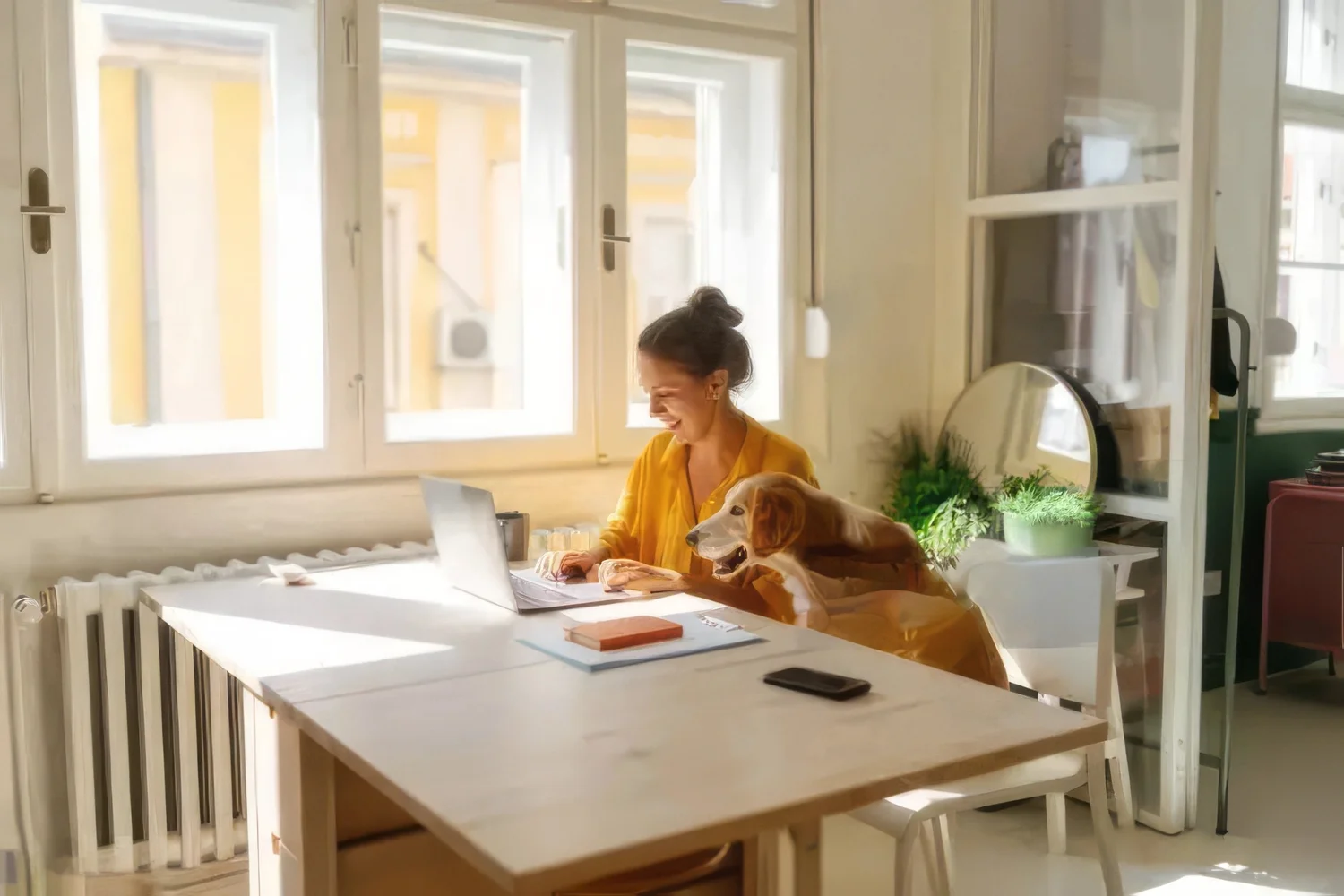 Photo of a young woman who is working from her home office, having the cutest and the cuddliest assistant - her pet dog.
