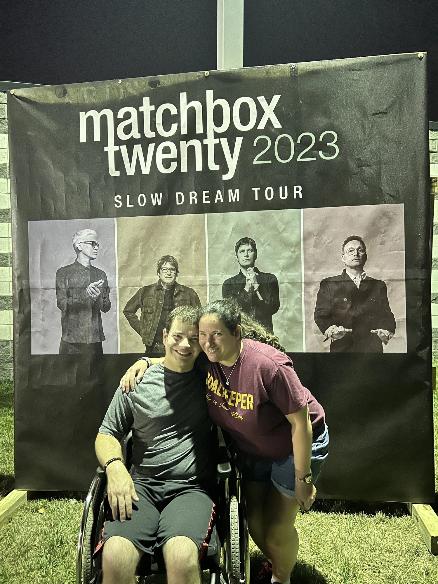 Ryan and Rachael smile in front of a Matchbox 20 Concert Poster at Jiffy Lube Live on July 27, 2023