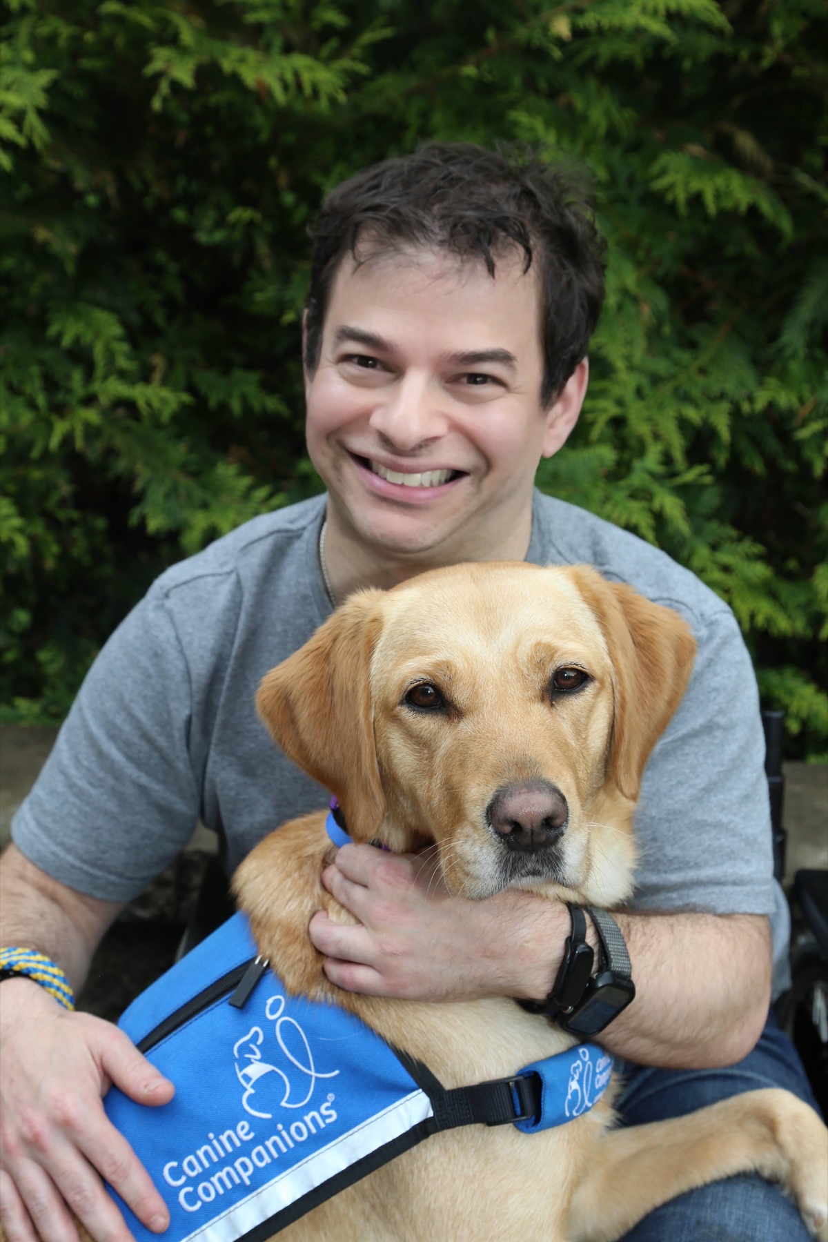 Ryan smiling behind Lovey, his yellow Labrador service dog, outdoors