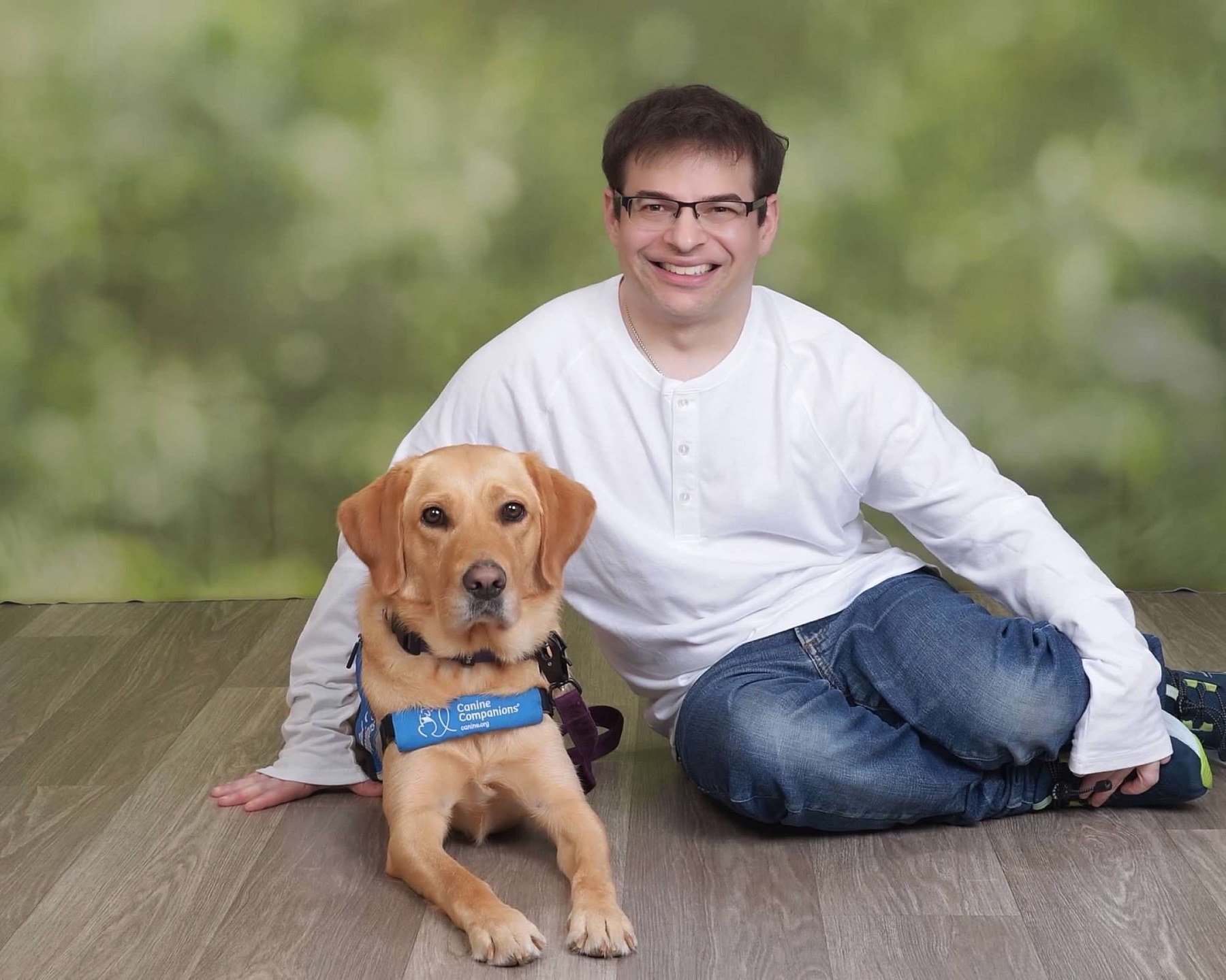 Ryan seated beside Lovey in her blue Canine Companions service-dog vest, both fully visible